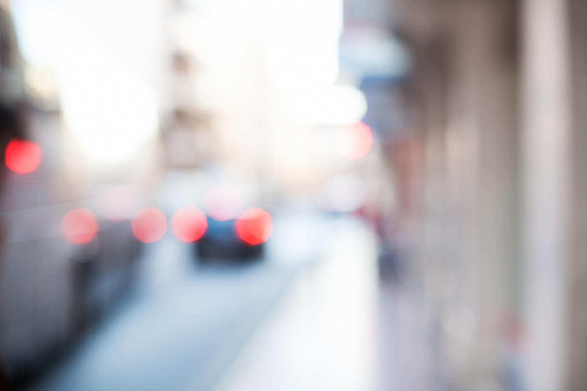 Unscharfe Aufnahme einer Stadtstraße mit Fahrzeugen und Gehweg bei Tageslicht.