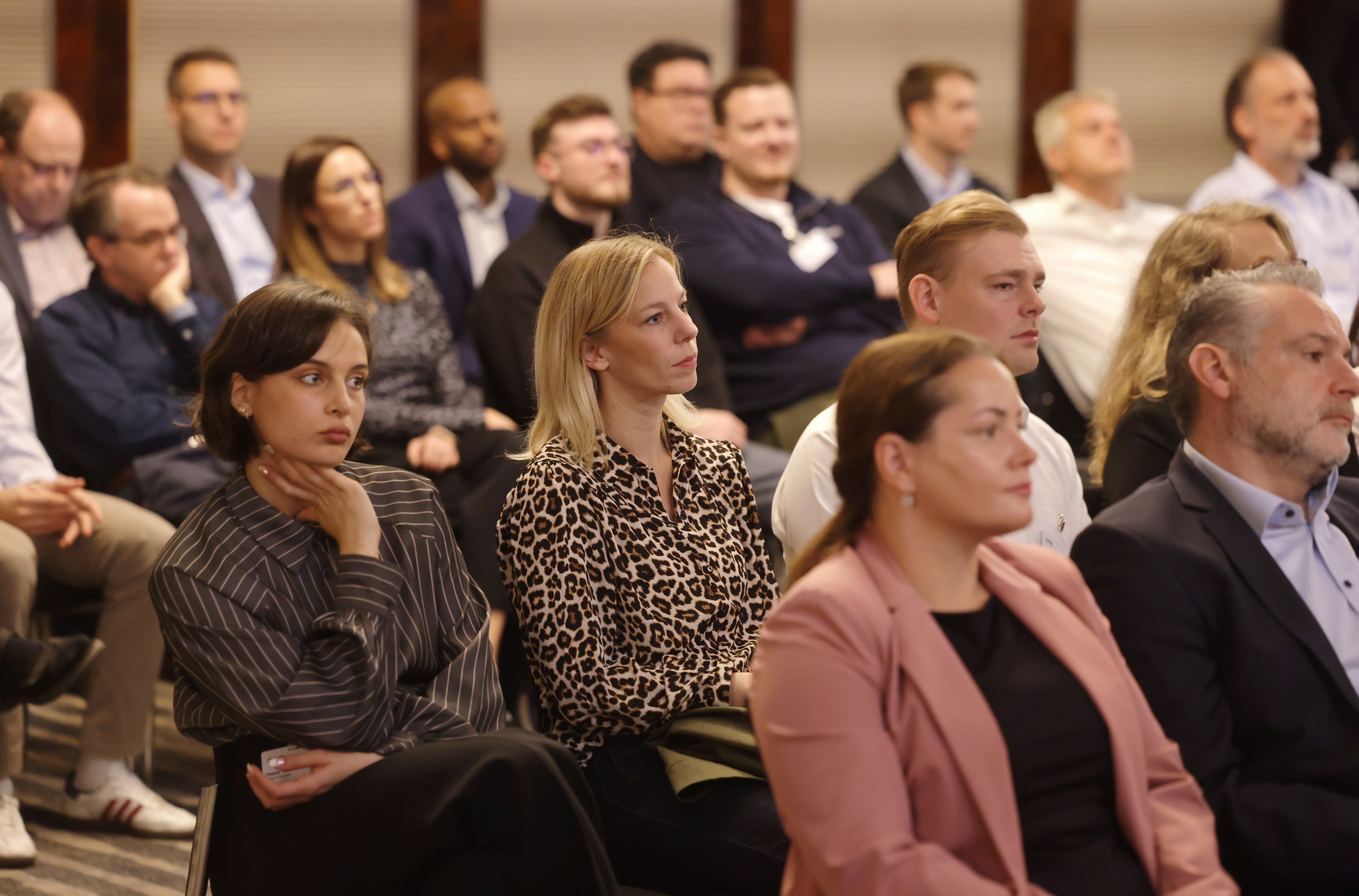 Menschen unterschiedlicher Altersgruppen sitzen aufmerksam in einem Konferenzraum und hören einem Vortrag zu.