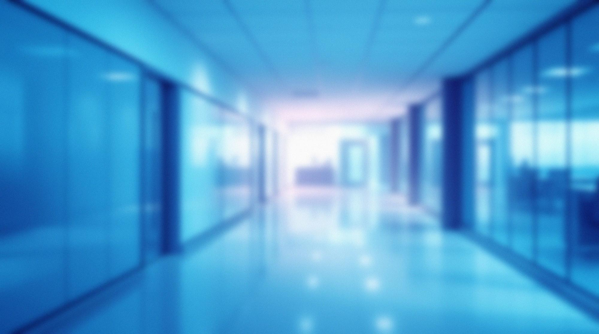 Unscharfer moderner Büroflur mit Glaswänden und reflexivem Boden.