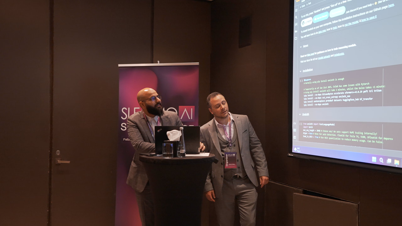 Zwei Männer in Anzügen präsentieren Programmiercode auf einer Leinwand bei einer Konferenz.