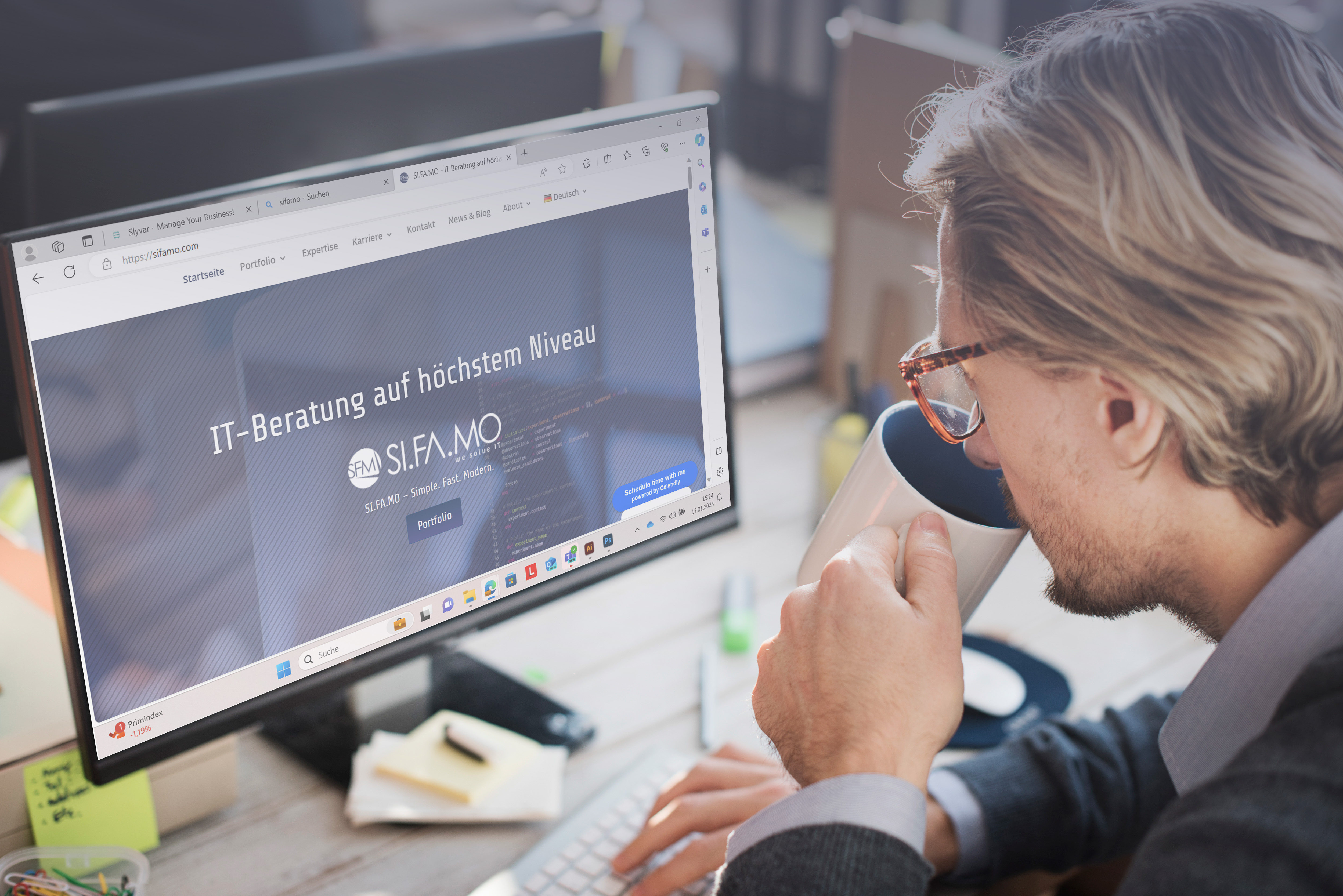 Mann mit Brille, der am Schreibtisch sitzt, eine Tasse hält und eine Website für IT-Beratung auf einem Computermonitor betrachtet.